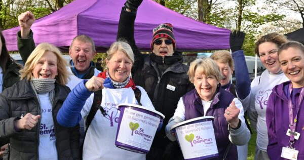 A group of men and women fundraising for St Gemma’s Hospice, holding donation buckets and cheering.
